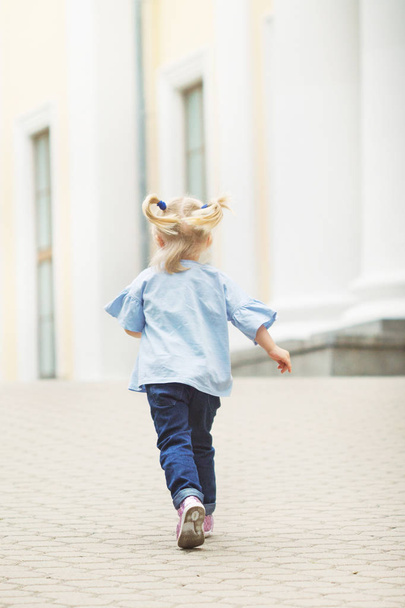 cheerful little blonde with two tails walking along the alley in the city park in summer sunny weather - Foto, immagini