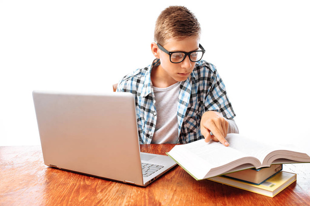 Jeune étudiant faisant des cours avec ordinateur portable et livres assis à table dans Studio
 - Photo, image