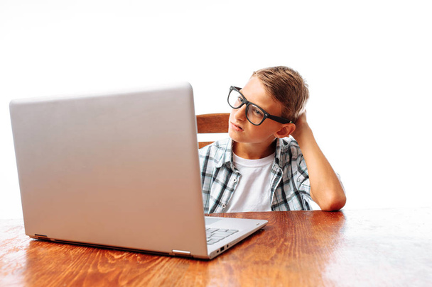 A young man resting after school sitting at the table and watching a movie on a laptop, throwing his hands behind his head, on a white background, in Studio - Фото, изображение