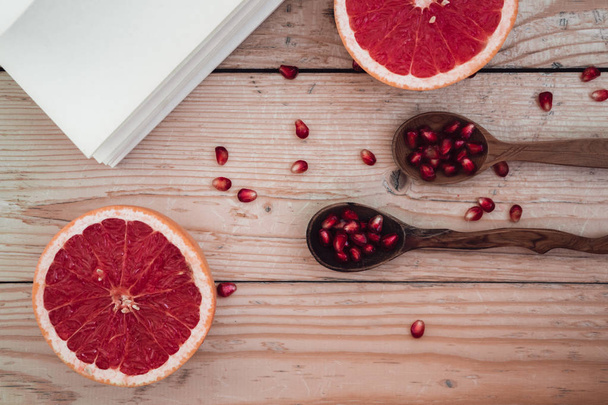 Pomegranate seeds in spoon with grapefruit slices and a book on  - Foto, Bild