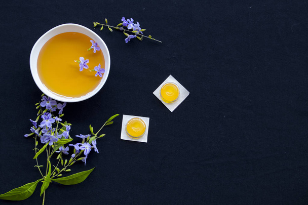 Husten Halsschmerzen Pastille Pillen aus Kräuterhonig Zitrone mit lila Blüten Arrangement auf schwarzem Hintergrund - Foto, Bild