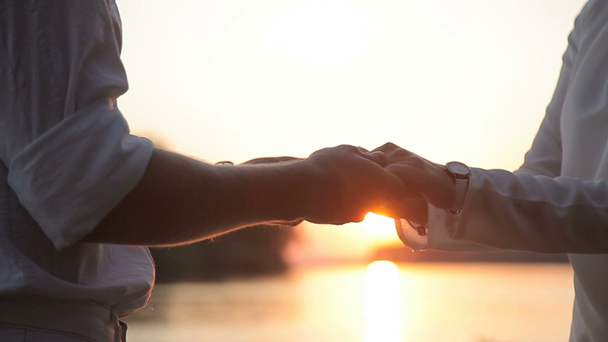 ein Kerl und ein Mädchen halten sich bei Sonnenuntergang an den Händen - Filmmaterial, Video