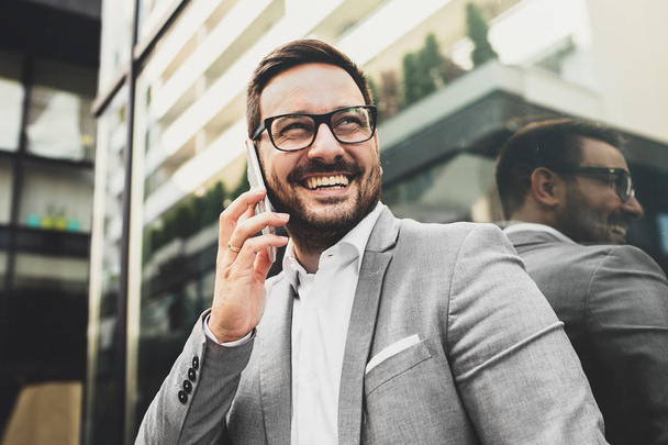 Young smiling businessman is using phone outside. - Foto, afbeelding
