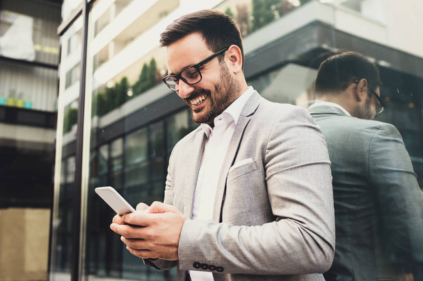 Young smiling businessman is using phone outside. - Photo, image