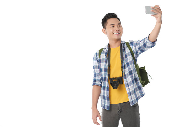 Веселий азіатських туристичних з рюкзак, беручи selfie сучасного смартфону стоячи проти білий фон, копія простір - Фото, зображення