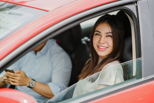 Nuoren japanilaisen aasialaisen naisen muotokuva, joka nojaa ulos punaisen auton ikkunasta ja hymyilee iloisesti
.  - Valokuva, kuva