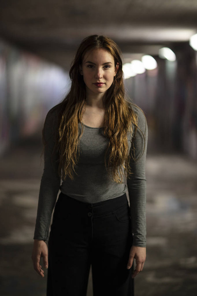 Портрет красивой молодой женщины, стоящей в городском подземном переходе. Три четверти длины. Селективный фокус
.  - Фото, изображение