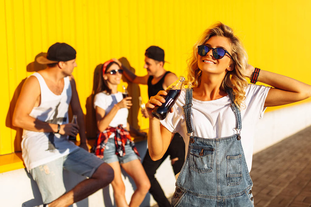 a group of young people with glass bottles with a drink stand near the supermarket, on a yellow background, friends come off in full, cheerful mood, Sunny day, Lifestyl concept, catch moments together with best friends - Foto, immagini