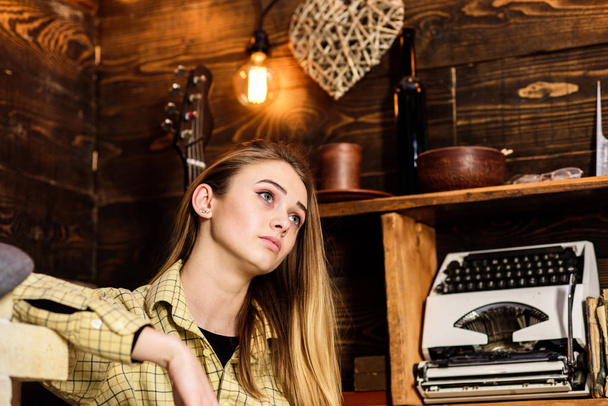 Tomboy concept. Lady on dreamy face in plaid clothes looks cute and casual. Girl in casual outfit in wooden vintage interior. Girl tomboy spend time in house of gamekeeper - Fotografie, Obrázek