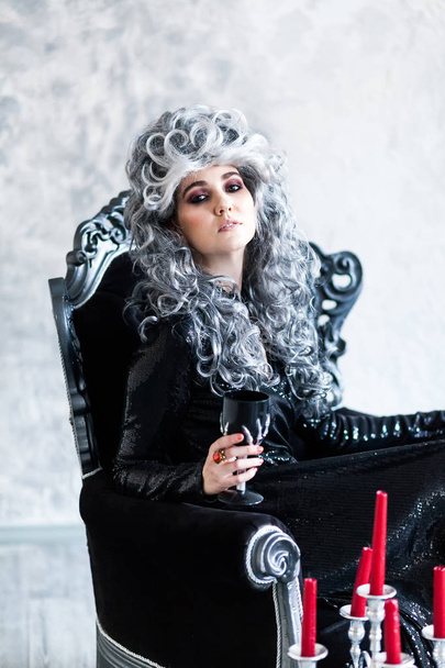 Halloween. Porträt einer hinreißenden jungen Glamour schöne Frau Vampir barocke Aristokratenhexe in schwarzem Kleid mit grauem lockigem Haar mit schwarzem Glas in der alten Burg. - Foto, Bild