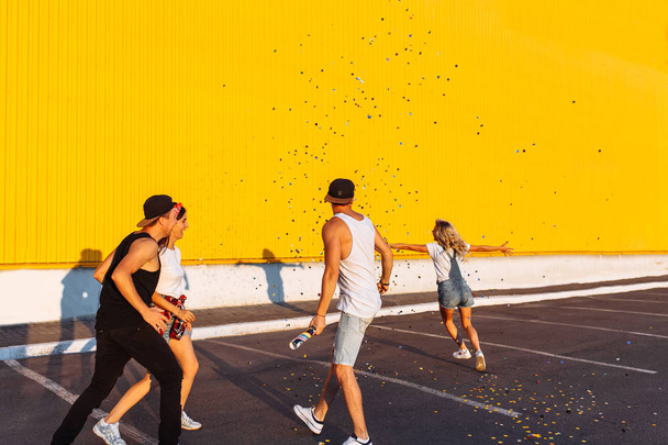 Beautiful cool young jump with confetti on a yellow background, a group of young people celebrating and having fun, summer mood, friends walking in the city in place, party in the Parking lot - Фото, изображение