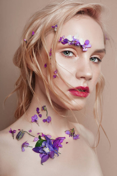 Portrait of a blonde woman with flower petals on her face close-up, bright red makeup and lipstick. Skin hydration, face care, anti-aging effect of cosmetics - Foto, immagini