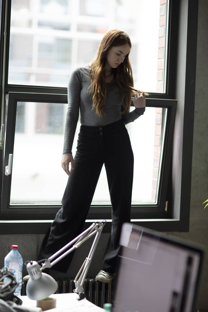 Girl standing on a office radiator. Daylight coming through from the window behind. Full length. Selective focus.  - Foto, imagen