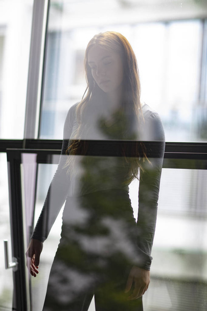 Ελκυστική γυναίκα στέκεται ανάμεσα σε παράθυρο του γραφείου και του γυαλιού σε ένα σχεδόν silhouetted εικόνων σκιαγραφεί την κομψή μορφή του γυναικείου σώματος. Μήκος τριών τετάρτων. Επιλεκτική εστίαση.  - Φωτογραφία, εικόνα