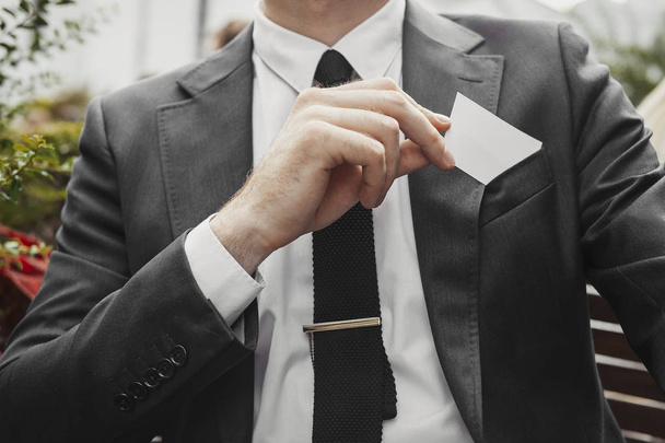 Close up of businessman putting blank business card in his jacket pocket. - Photo, image