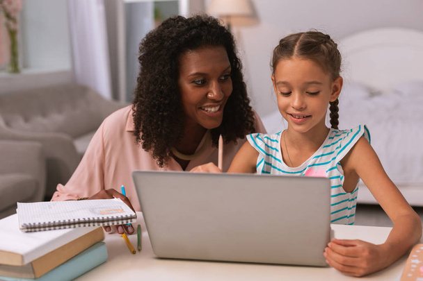 Delighted nice woman helping her daughter with homework - Foto, imagen