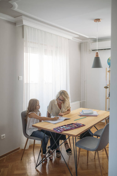 Cute Caucasian schoolgirl studying at home with her mother. - Fotografie, Obrázek
