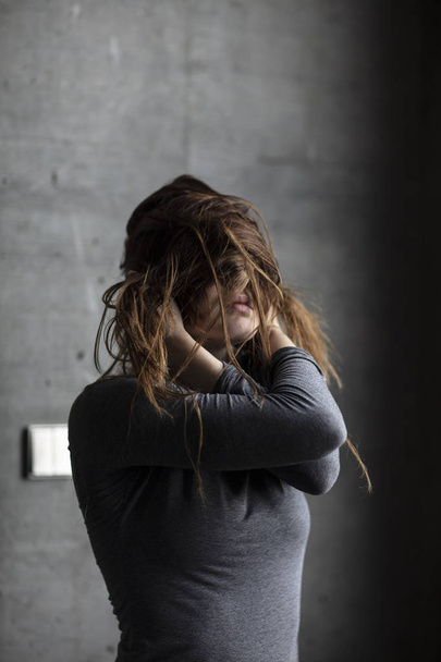 Modelo femenina posando detrás de una pared de hormigón gris oscureciendo su cara con su propio pelo. Tiro medio
.  - Foto, imagen