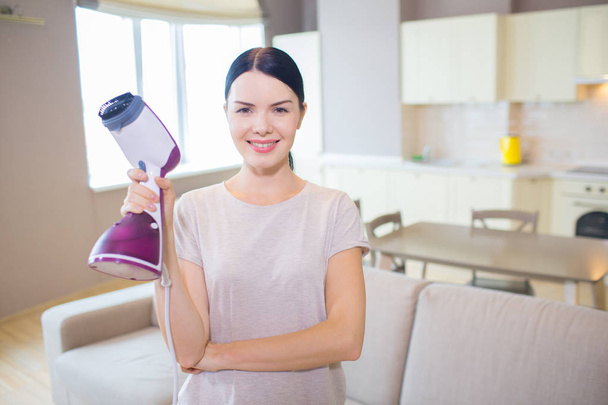 Pretty woman stands with small vacuum cleaner in hand and poses on camera. She has finishes cleaning. Girl looks happy. - Foto, Bild