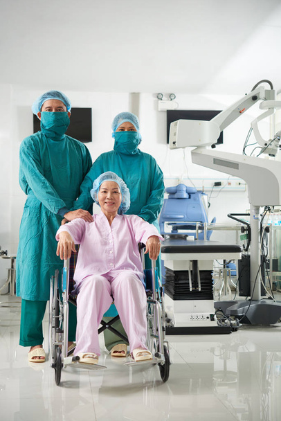 Зрелая азиатка, сидящая в инвалидной коляске с профессиональными хирургами
 - Фото, изображение