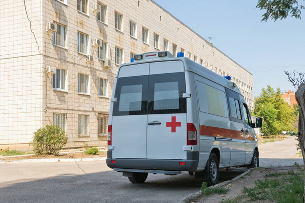 A new white ambulance van is parked next to the hospital complex - Foto, afbeelding