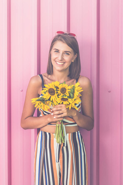 Portrait of happy woman with sunflowers bouquet against rose wall outdoors. - Foto, Bild