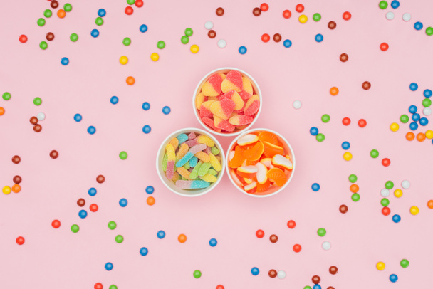 top view of paper cups with jelly candies and scattered dragee isolated on pink  - Photo, Image