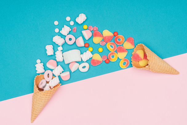 top view of jelly candies, marshmallows and waffle cones on blue and pink surface - Foto, Imagen