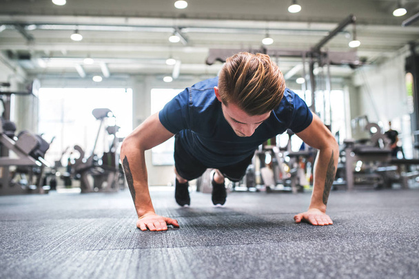 Young fit man in gym doing push ups. - Photo, Image