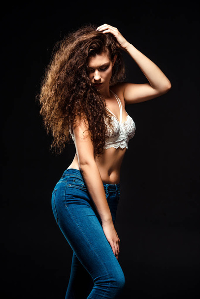 portrait of beautiful woman in white bra and jeans posing isolated  on black - 写真・画像