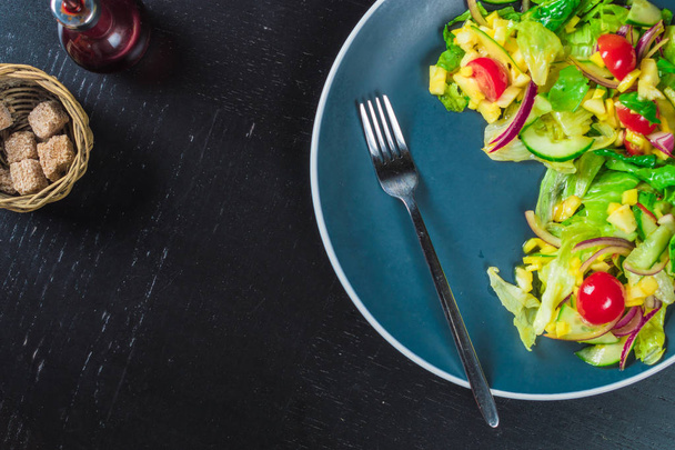 Assiette bleue de salade avec mangue, concombre et tomates cerises sur table noire
 - Photo, image