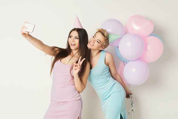 Two happy friends making selfie on smartphone at party - Foto, Imagen