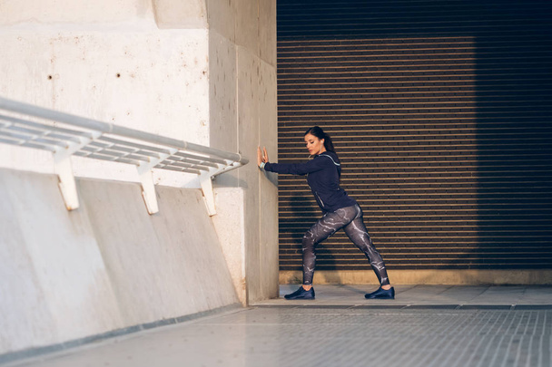 Urban sportowy młoda kobieta rozciąganie cieląt na rozgrzewkę przed ćwiczeniami. Trening fitness na zewnątrz miasta. - Zdjęcie, obraz