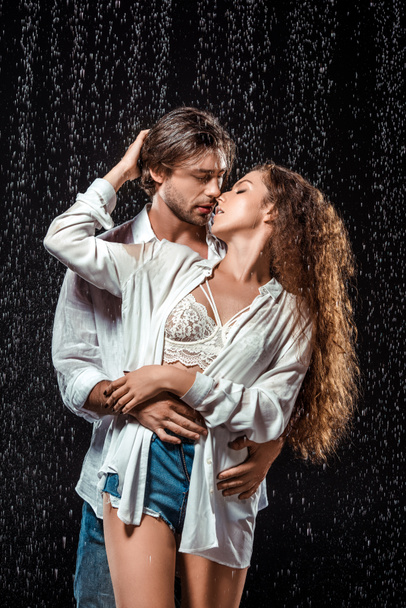 Porträt eines verführerischen Paares, das sich unter Regen auf Schwarz umarmt - Foto, Bild