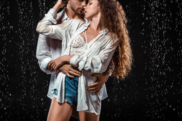 πορτρέτο της δελεαστική ζευγάρι αγκαλιάζει υπό βροχή που απομονώνονται σε μαύρο - Φωτογραφία, εικόνα