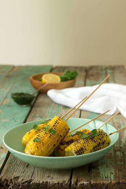 Sweet baked corn in a deep plate, served with chamichurri sauce and lemon. Rustic style, selective focus. - Photo, Image
