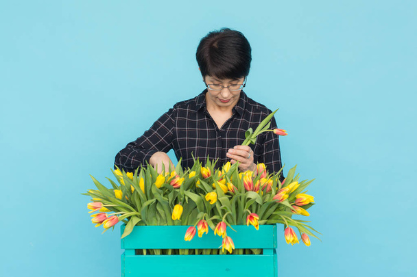 Šťastná žena středního věku s brýlemi drží pole tulipánů v modrém pozadí - Fotografie, Obrázek