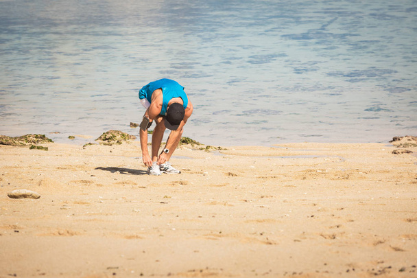 sportif avec brassard smartphone attachant lacets sur la plage près de la mer
 - Photo, image