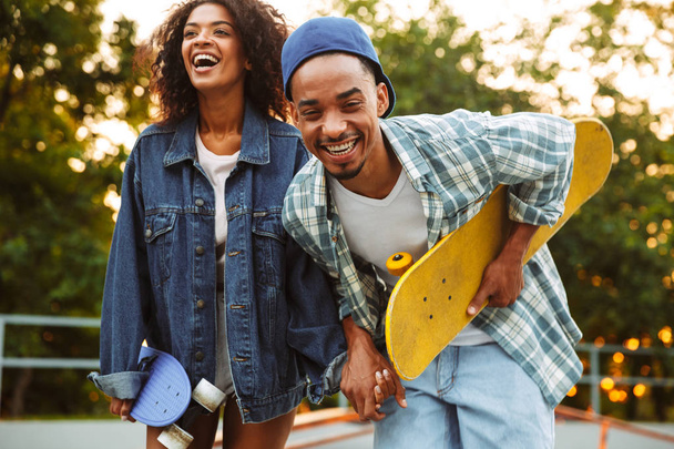 Portrait of an excited young african couple with skateboards having fun together at the skate park - 写真・画像