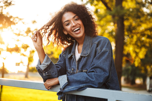 Happy young african girl in denim jacket spending good time at the park - Foto, imagen