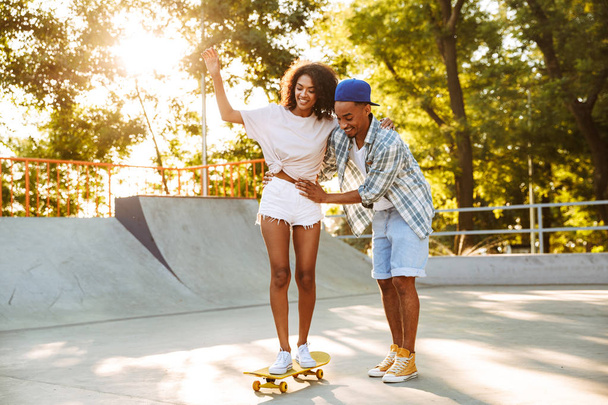 Portret uśmiechający się młodej pary Afryki z deskorolki, wspólna zabawa w skate parku, uczy się jeździć - Zdjęcie, obraz