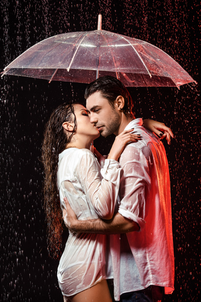 vue latérale du couple romantique en chemises blanches avec parapluie debout sous la pluie sur fond noir
 - Photo, image