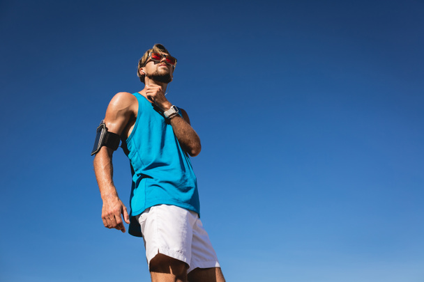 Blick von unten auf Sportler in Sonnenbrille mit Smartphone-Armbinde  - Foto, Bild