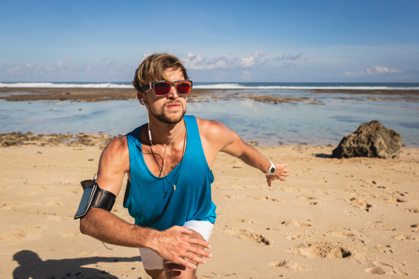 sportsman with smartphone armband working out on beach near sea - Valokuva, kuva