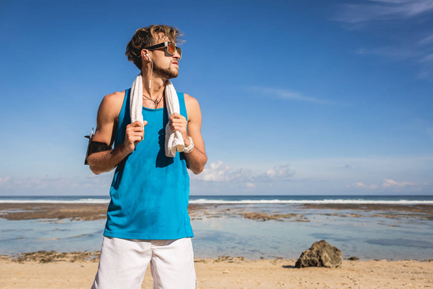 desportista bonito com toalha de pé na praia
 - Foto, Imagem