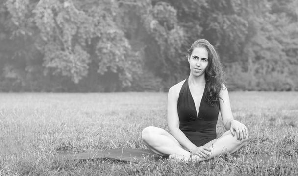 Young woman practicing yoga in nature. Sitting on green grass and meditating. Green background with toned effect. Healthy and sport concept.Copy space for text. - Foto, immagini