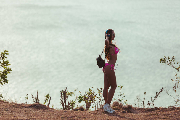 side view of attractive girl in headphones and pink bikini standing on coastline - Foto, Imagen