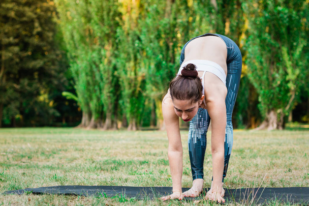 schlanke junge Frau, die Yoga in der Natur praktiziert und in verschiedenen Yogapositionen steht. grüner Hintergrund, tief gestreckt. gutes gesundes und sportliches Konzept.  - Foto, Bild