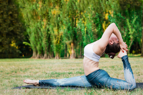 Štíhlá mladá žena cvičí jóga v přírodě, stojící v různých jógových pozic. Zelené pozadí, hluboké strečink. Dobré zdraví a sport koncept.  - Fotografie, Obrázek