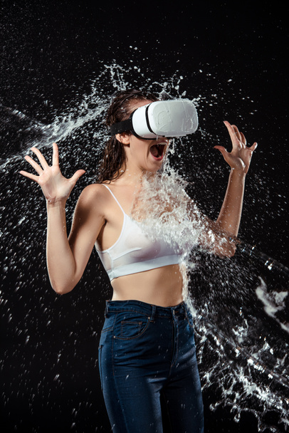 emotionele vrouw in vr headset swilled met water geïsoleerd op zwart - Foto, afbeelding